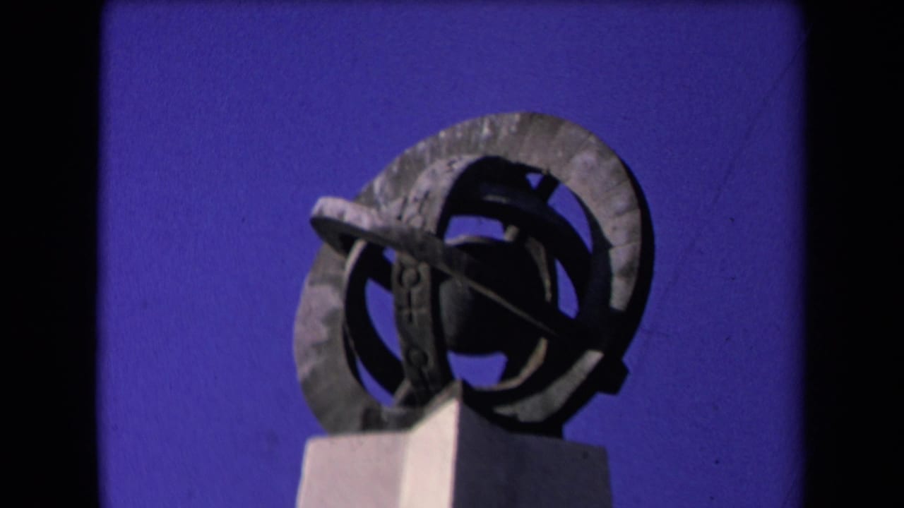 Geometric metal sculpture with circular forms on a pale pedestal against a blue sky.