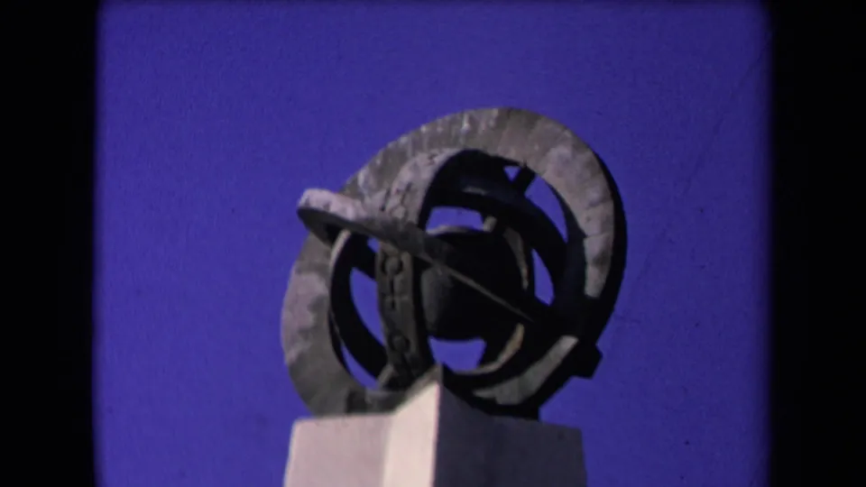 1967 Los Angeles 8mm frame showing a weathered abstract metal sculpture on a pedestal against a deep blue sky.