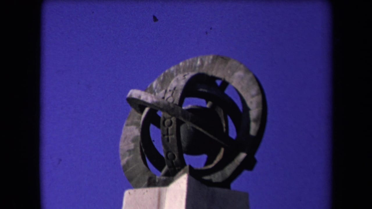 Abstract circular metal sculpture on a pedestal, framed tightly against clear blue sky.
