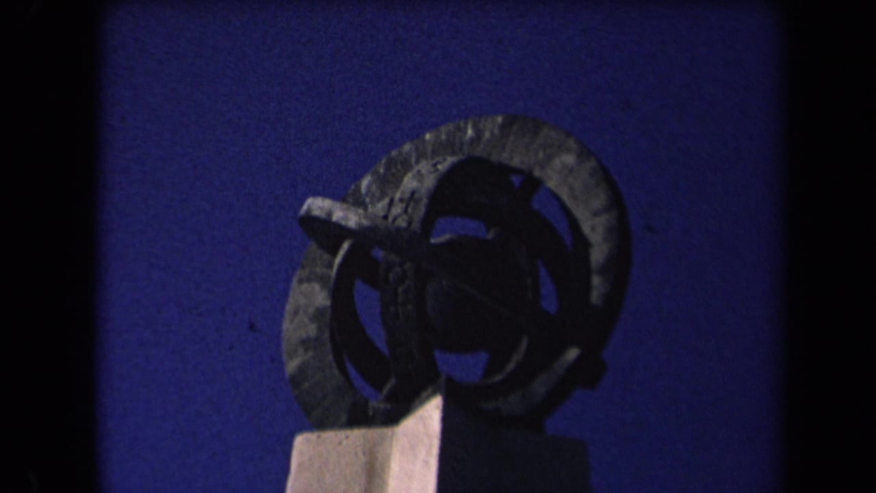 Sculptural form or monument against a blue background, partly obscured by film borders.