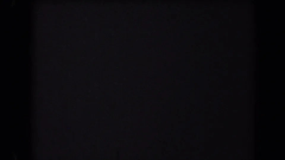 A very dark 8mm frame with film grain and edge shadows, suggesting a brief underexposed or obscured moment in the clip.