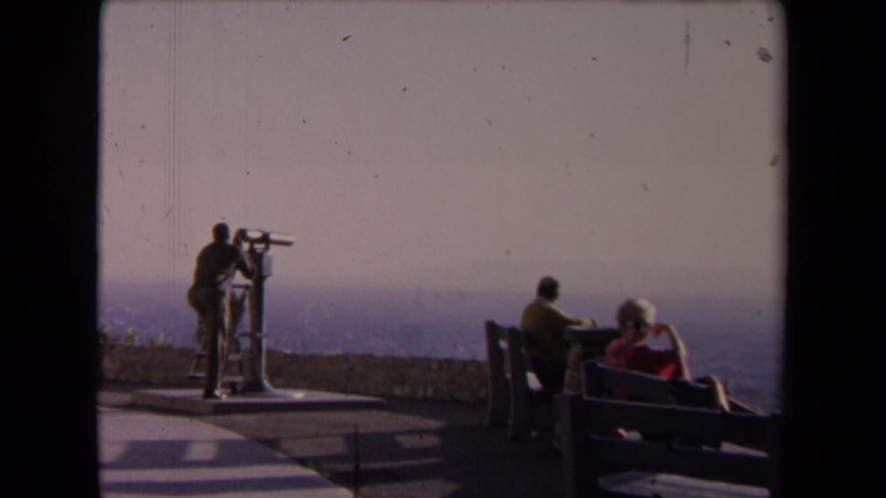 Visitors on an observatory deck with benches and a coin-operated telescope overlooking a hazy landscape.