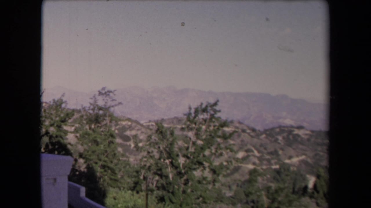 1967 Los Angeles scenic view from an elevated deck, with trees, hills, distant mountains, and a low white wall.