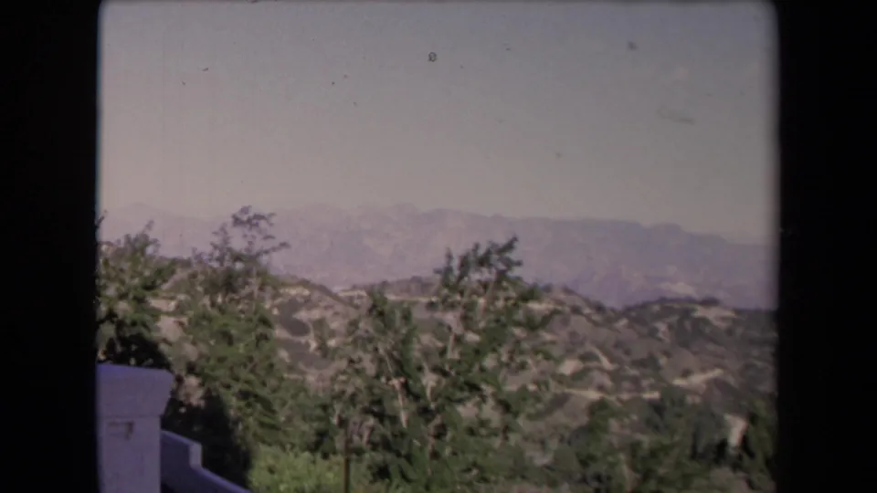 1967 Los Angeles scenic view from an elevated deck, with trees, hills, distant mountains, and a low white wall.