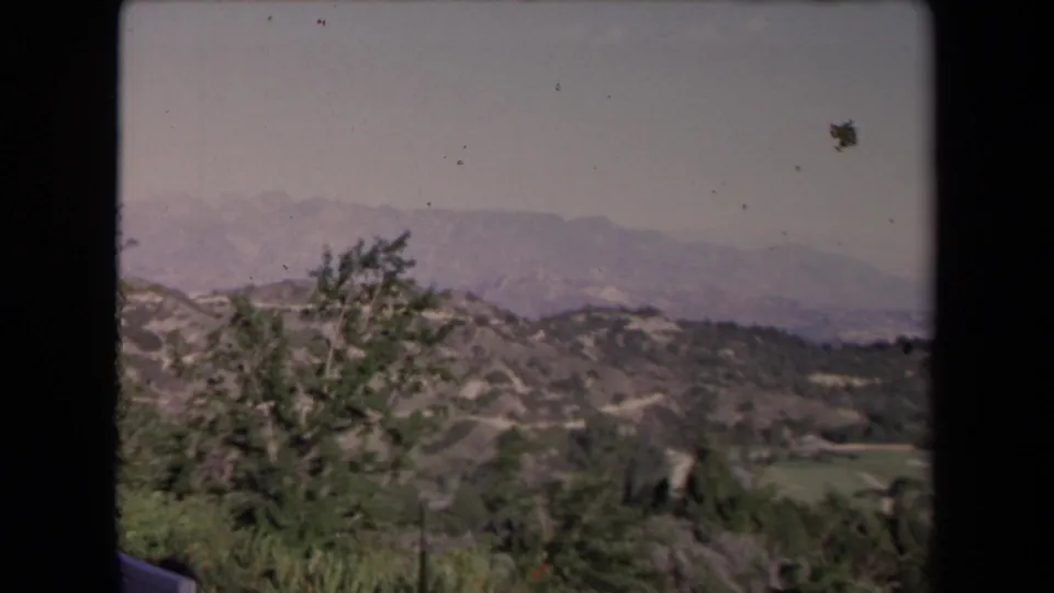 1967 Los Angeles scenic overlook frame with trees in the foreground and layered hills and mountains in the distance.