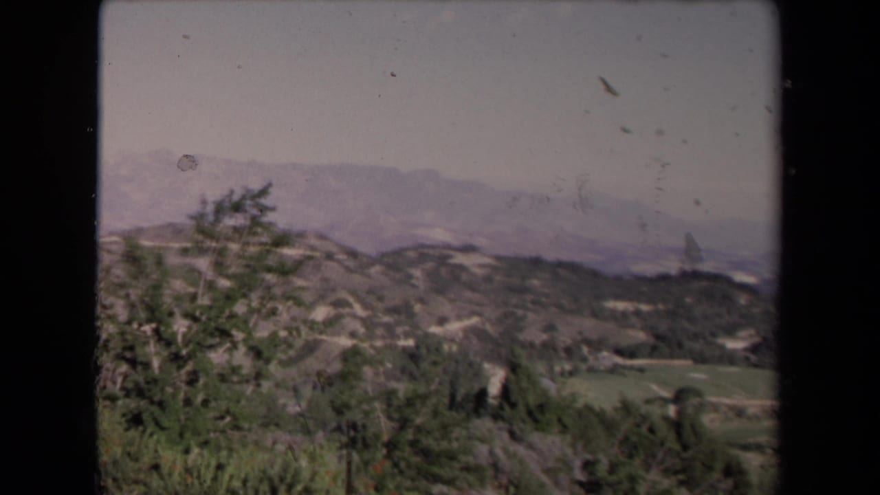 Scrub-covered hills with green fields and hazy mountains beyond.