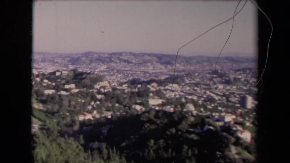 1967 Los Angeles home-movie frame showing a soft-focus city panorama, hillside homes, roads, trees, and visible film wear.