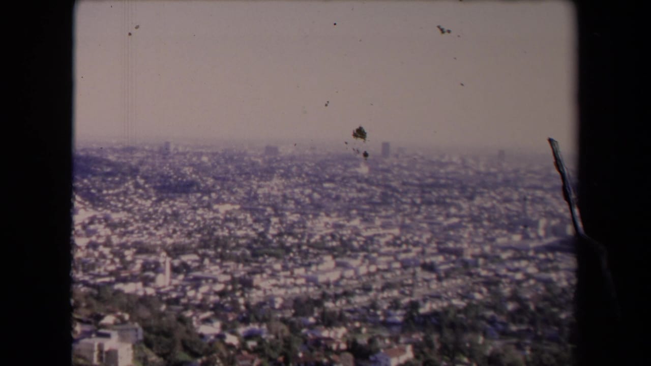 1967 Los Angeles panorama from a high viewpoint, showing sprawling neighborhoods, haze, and visible film dust and edge marks.