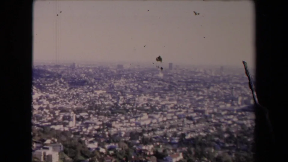 1967 Los Angeles panorama from a high viewpoint, showing sprawling neighborhoods, haze, and visible film dust and edge marks.
