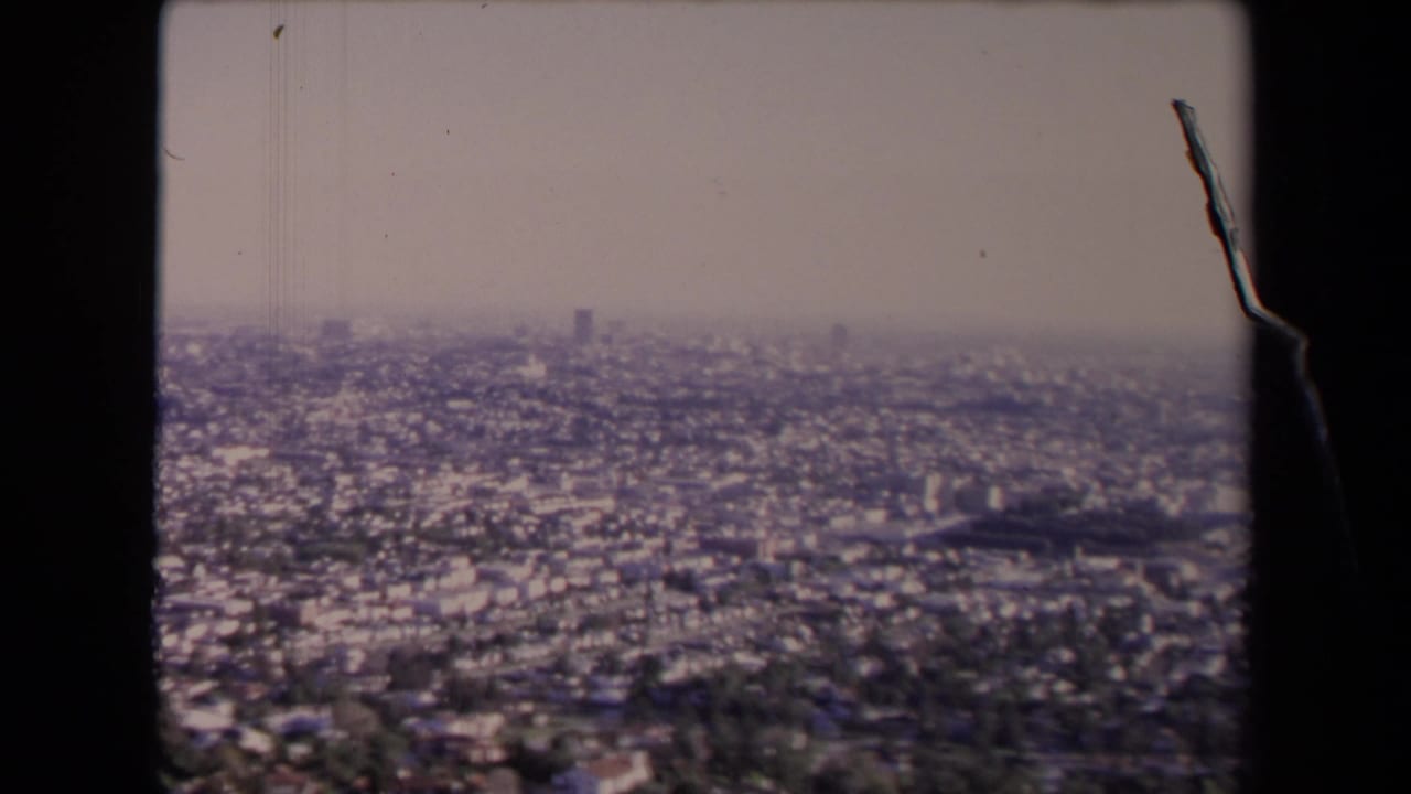 Hazy elevated view over a dense cityscape with low-rise buildings and distant skyline.