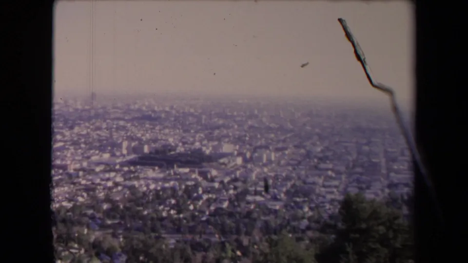 Home-movie frame of Los Angeles in 1967, looking across a broad urban area from a hillside or overlook with haze, grain, and visible surface marks.