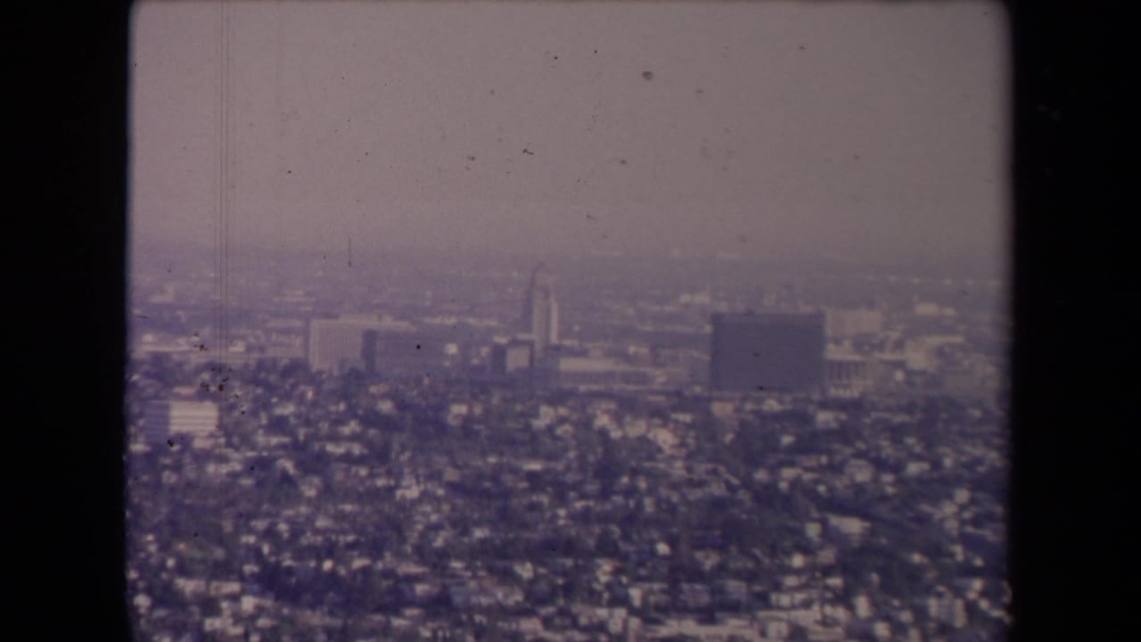 Aerial cityscape with haze, residential blocks, and larger buildings in the distance.