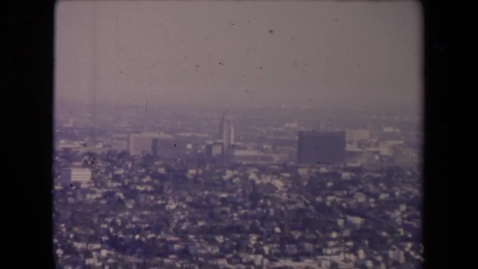 Los Angeles, 1967, seen from above through haze with residential blocks, distant towers, and muted 8mm color shift.