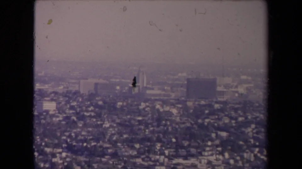 1967 Los Angeles aerial view showing dense neighborhoods and distant high-rises, with visible dust and scratches in the 8mm scan.