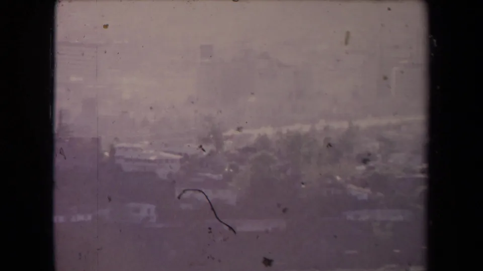 Hazy 1967 Los Angeles aerial frame with roads, tree cover, low buildings, and a faint skyline beyond.
