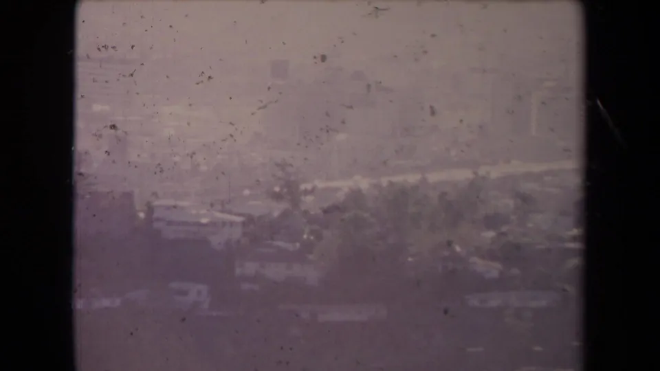 1967 Los Angeles aerial frame showing city blocks, roads, distant high-rises, and pronounced haze on aged 8mm film.