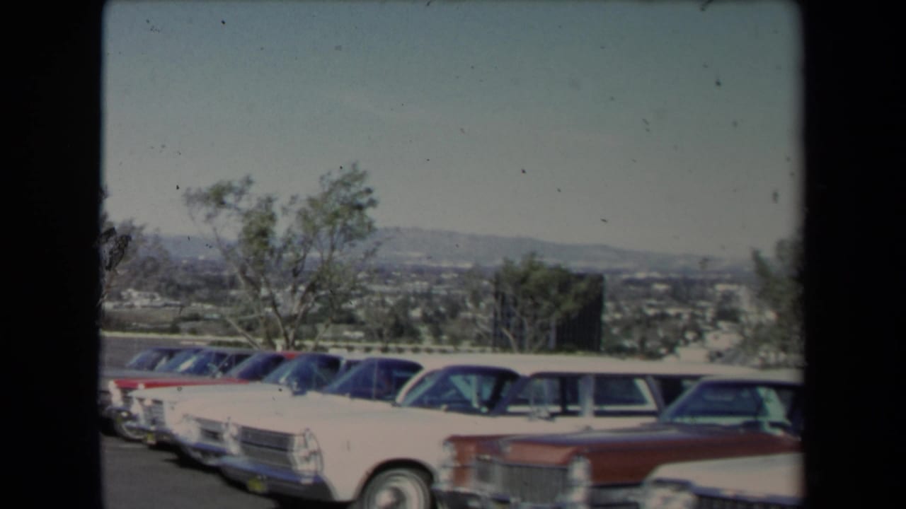 1967 Los Angeles 8mm frame showing classic American cars lined up on a hillside lot overlooking the city basin.