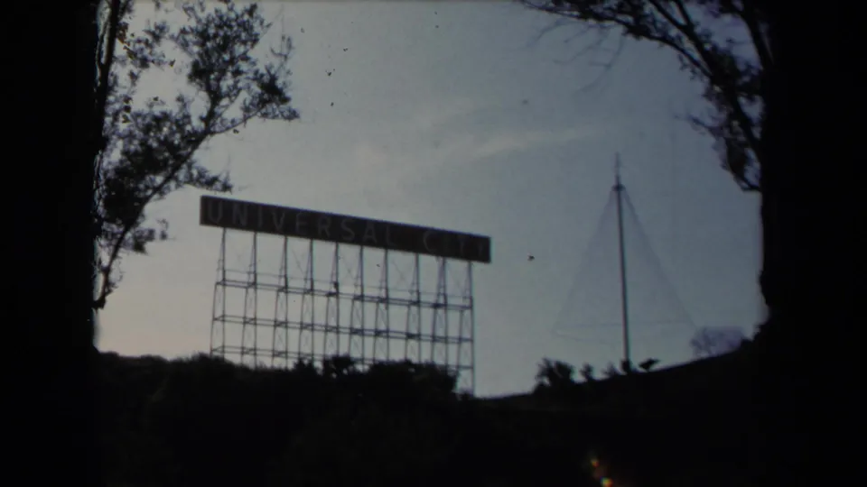 1967 Los Angeles-area home-movie frame showing the Universal City sign framed by trees and hillside shadow.