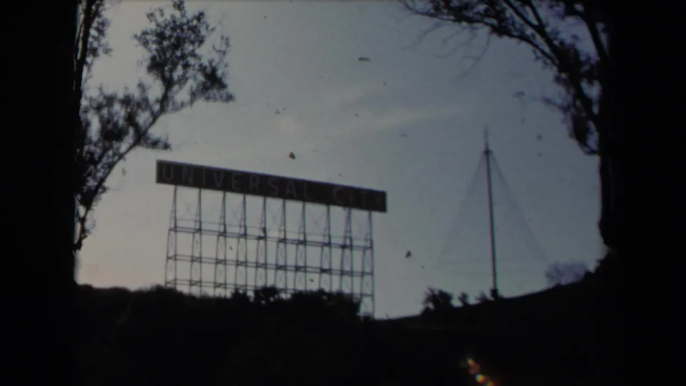 1967 Los Angeles-area frame with the Universal City sign partially framed by trees and small-gauge film edge shadows.