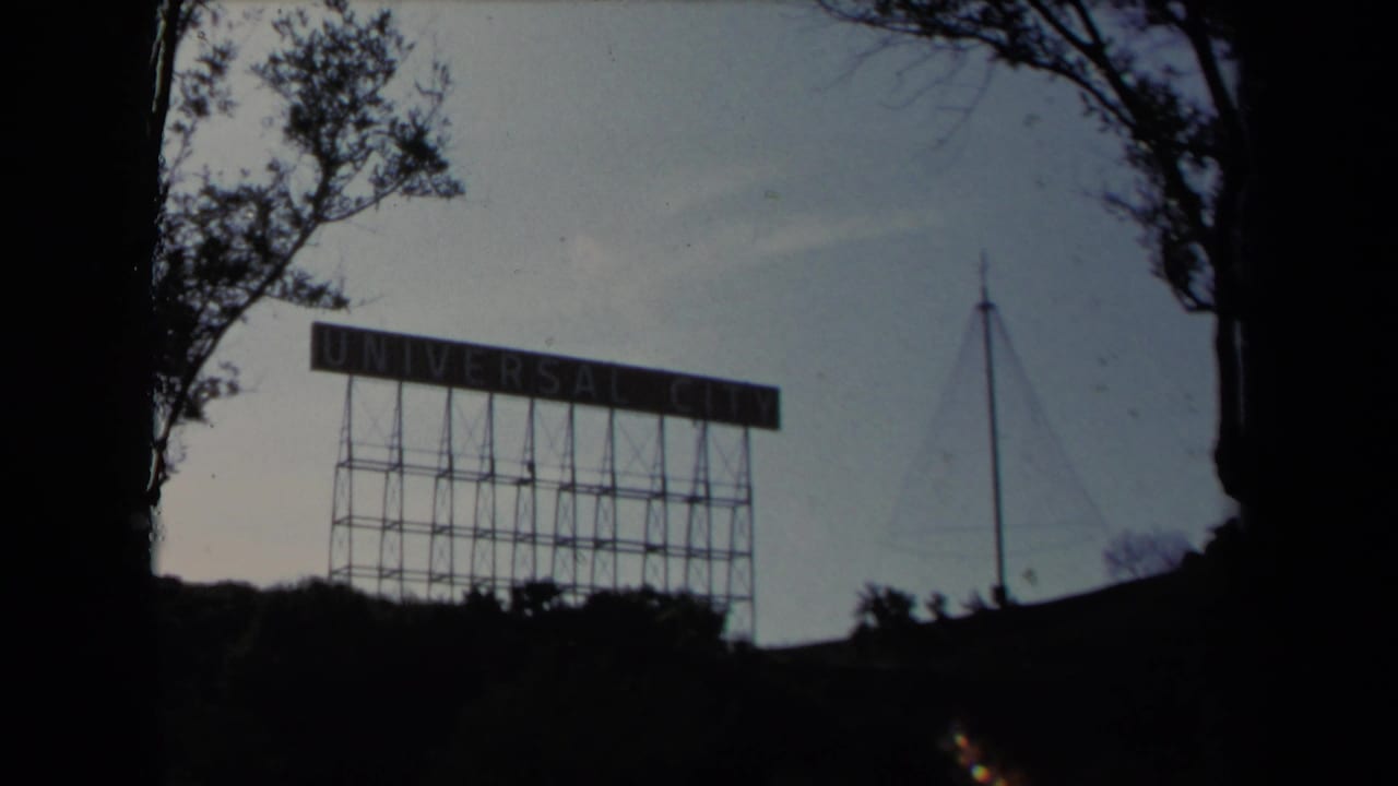 Universal City sign silhouetted behind trees and hillside.