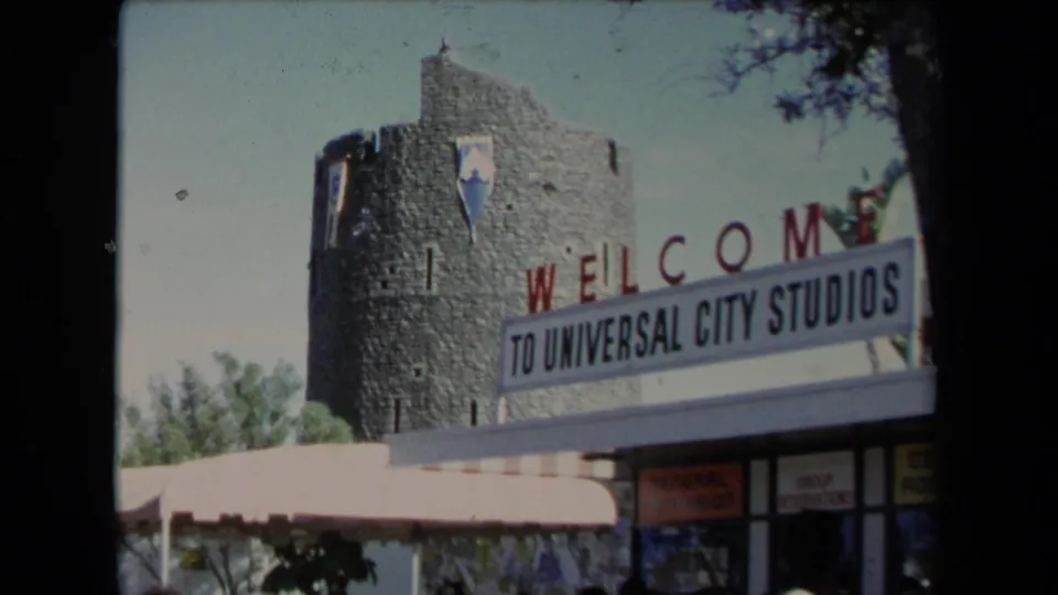 1967 exterior view of a stone tower and Welcome to Universal City Studios sign at Universal City in Los Angeles.