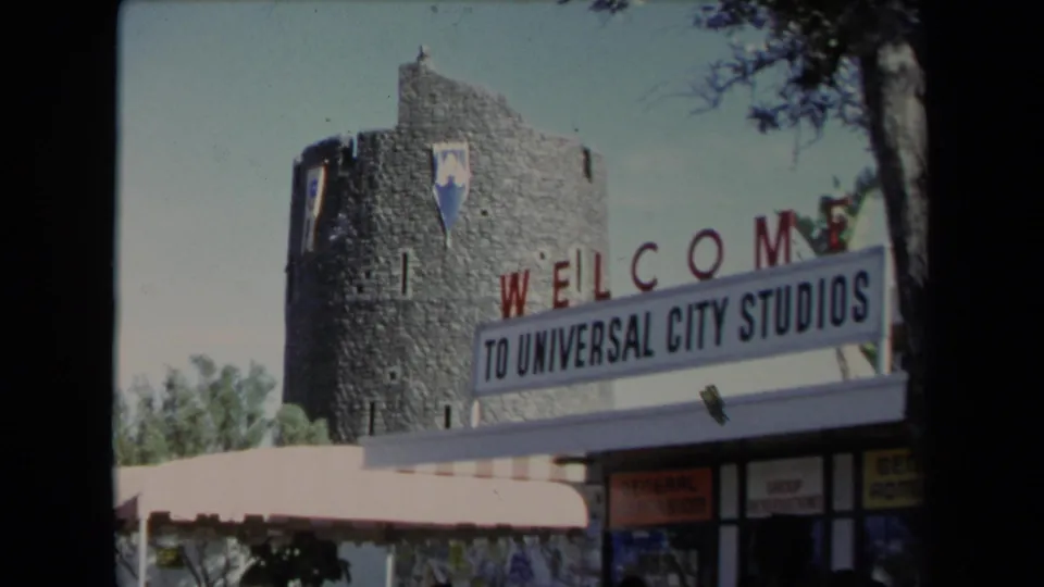 Bright 1967 8mm view of the Universal City Studios welcome sign, stone tower, awning, and entrance frontage in Los Angeles.