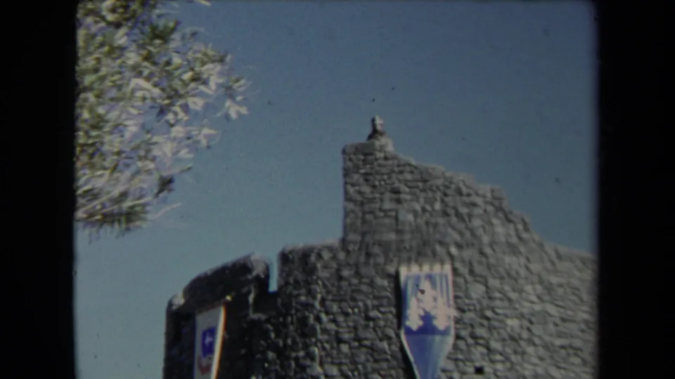 1967 Los Angeles 8mm frame showing the themed stone tower and banner at Universal City Studios from a closer visitor angle.