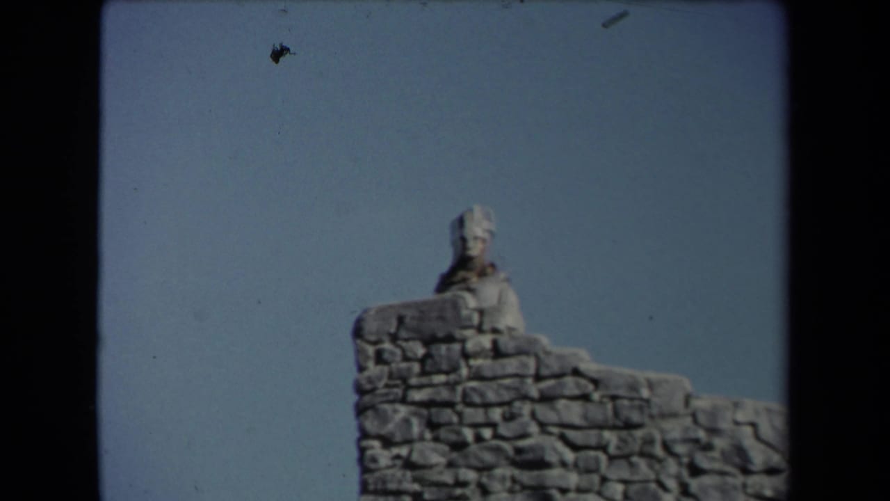Similar view of a pale figure behind a stone wall with open sky.