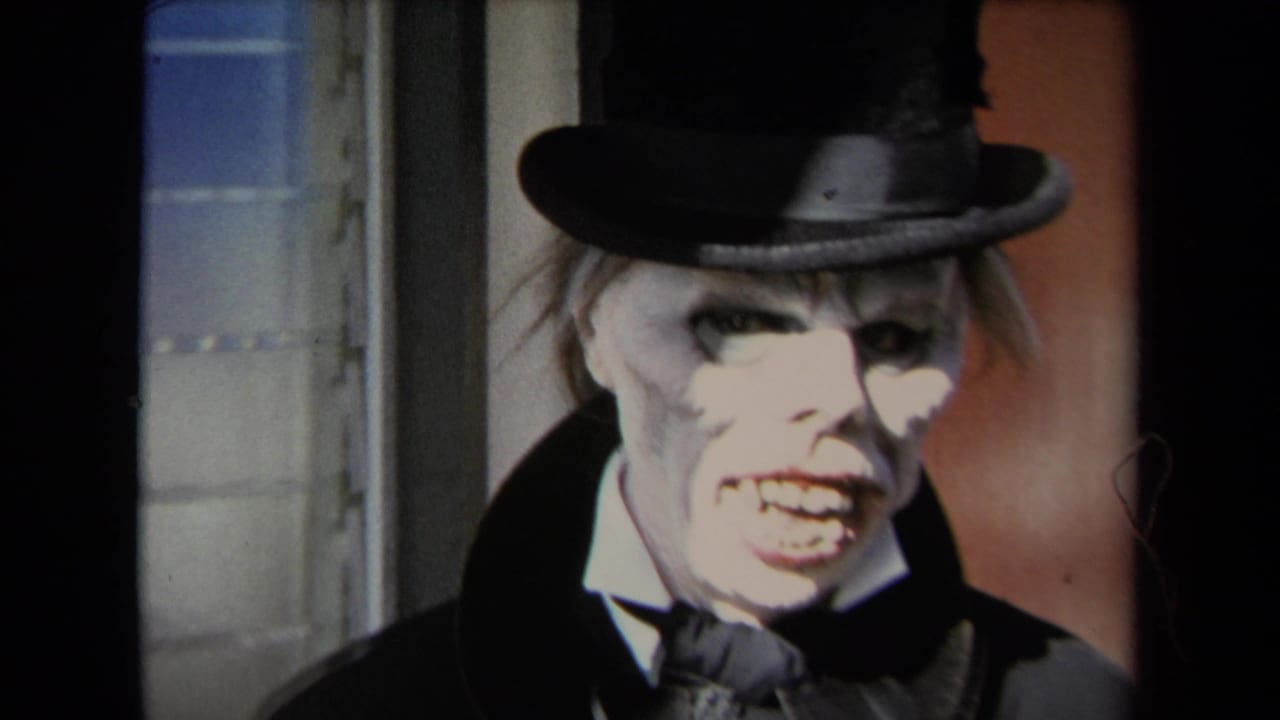 1967 Los Angeles 8mm frame of a person in ghoul-like makeup, black top hat, white collar, and dark coat near a doorway.