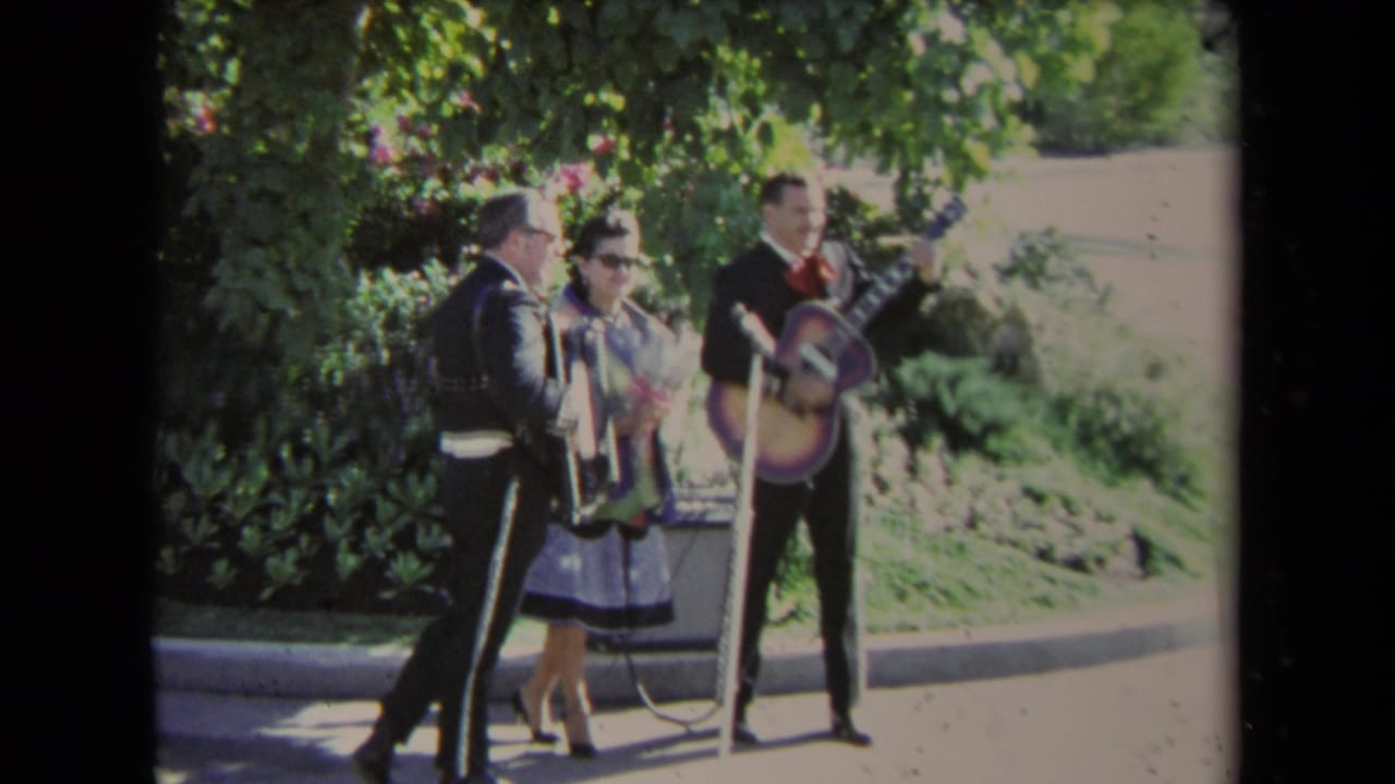 Three mariachi musicians perform outdoors while a woman in sunglasses stands nearby.