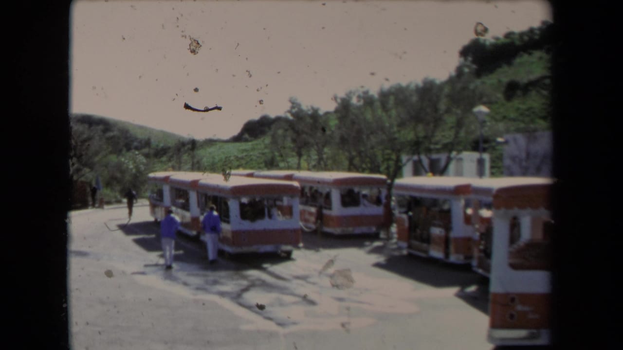 Several open-air tour buses line a paved area with visitors near the center.