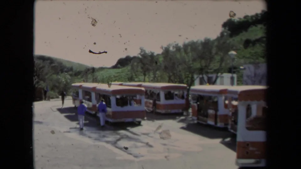 1967 Los Angeles footage frame with a line of orange-and-white tour buses and small figures walking in a tourist area.