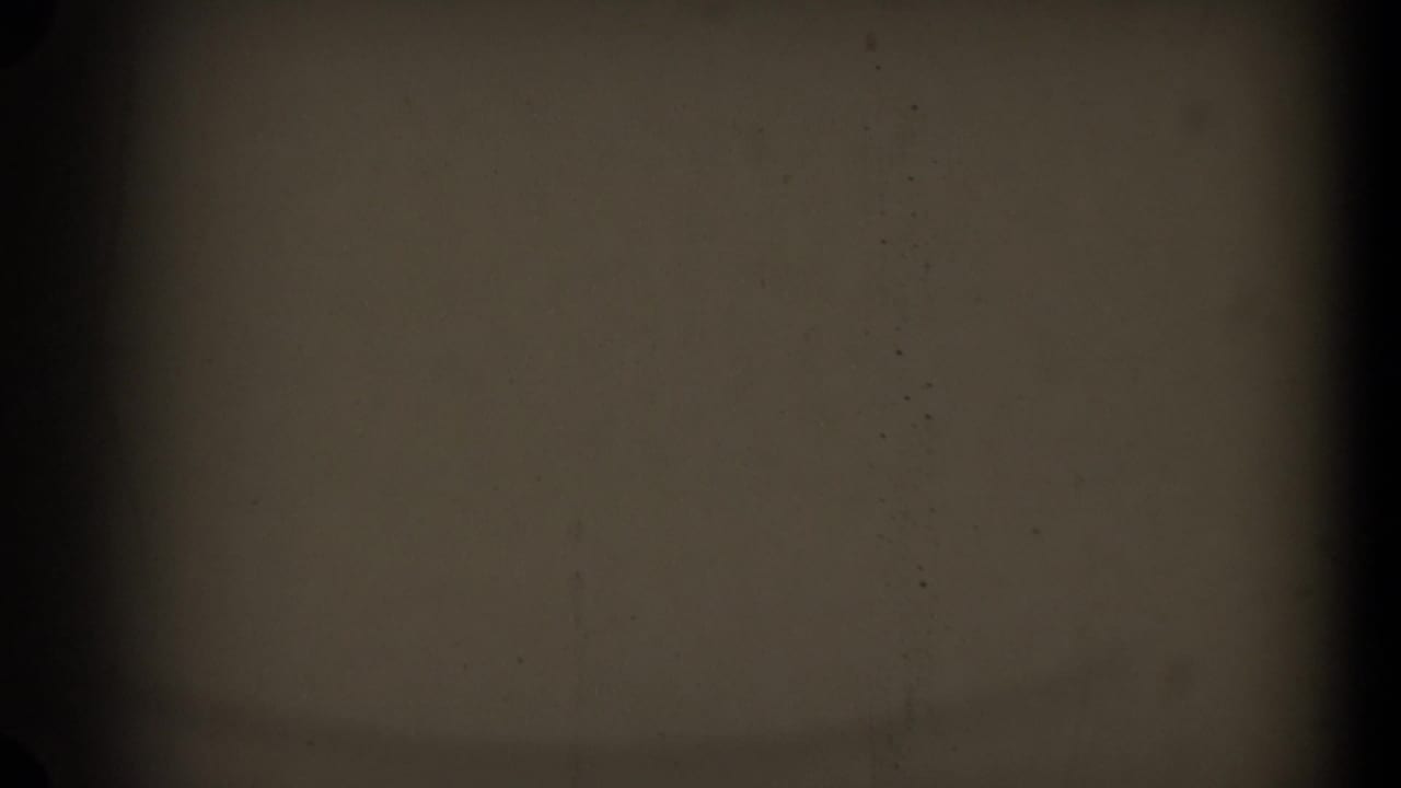 A mostly obscured 8mm frame with dark borders, central vertical banding, and faint film texture before the sidewalk scene appears.