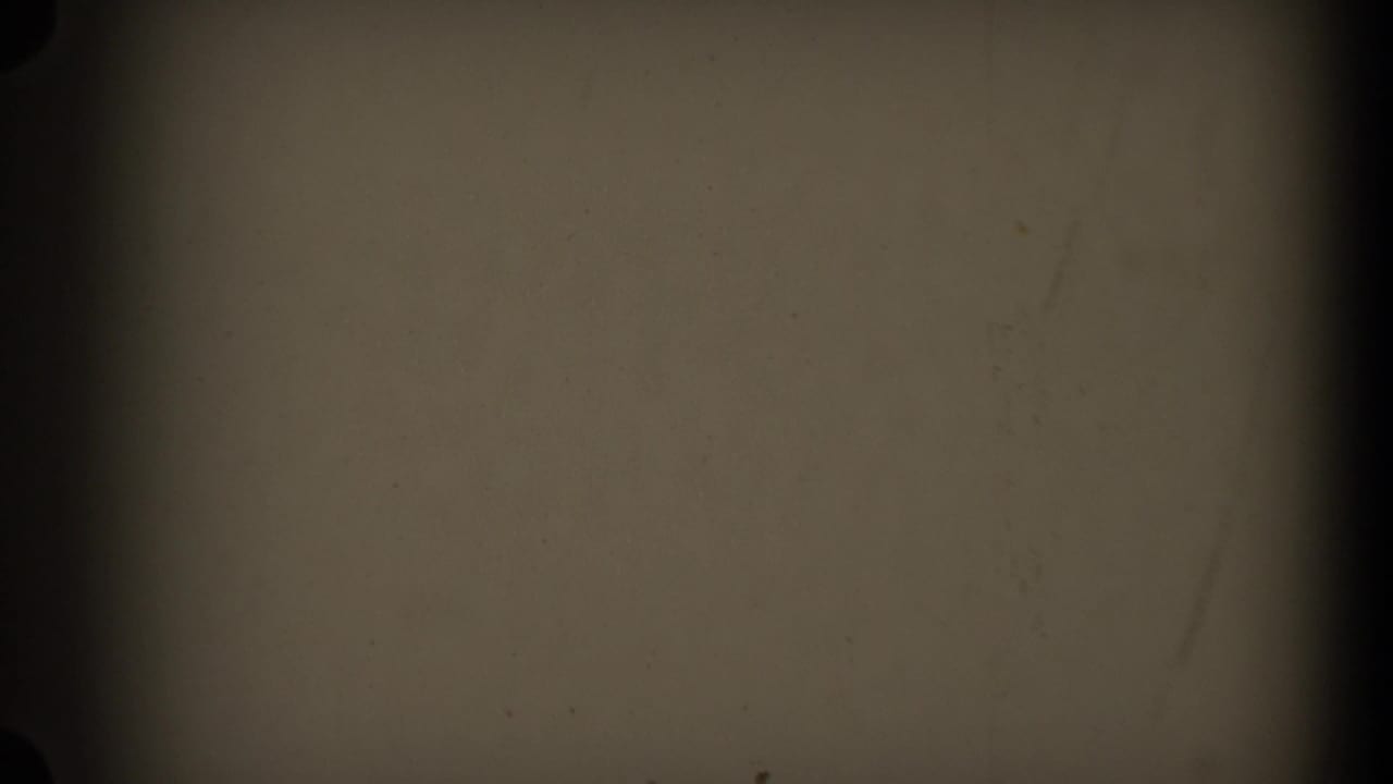 A second mostly obscured 8mm frame showing film texture, dark edge shadows, and limited visible scene detail.