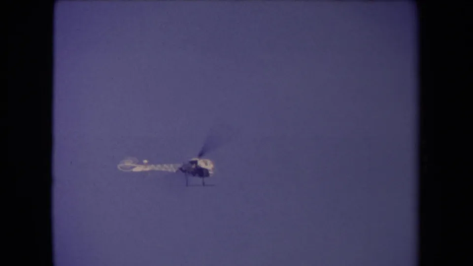 A lone helicopter is held in view against open sky, with the home-movie scan showing soft focus and muted color.