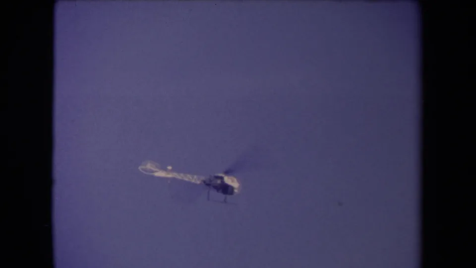 The helicopter appears near the lower frame edge, still moving through the blue Los Angeles sky in the 8mm clip.