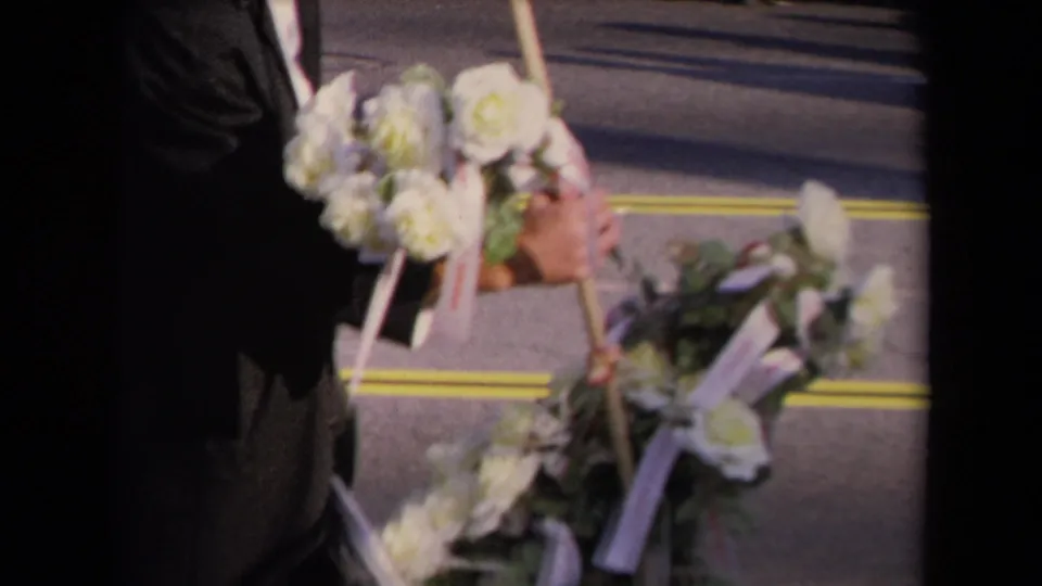 Close 8mm view of white floral wreaths and ribbons being handled during a 1967 Los Angeles memorial scene.