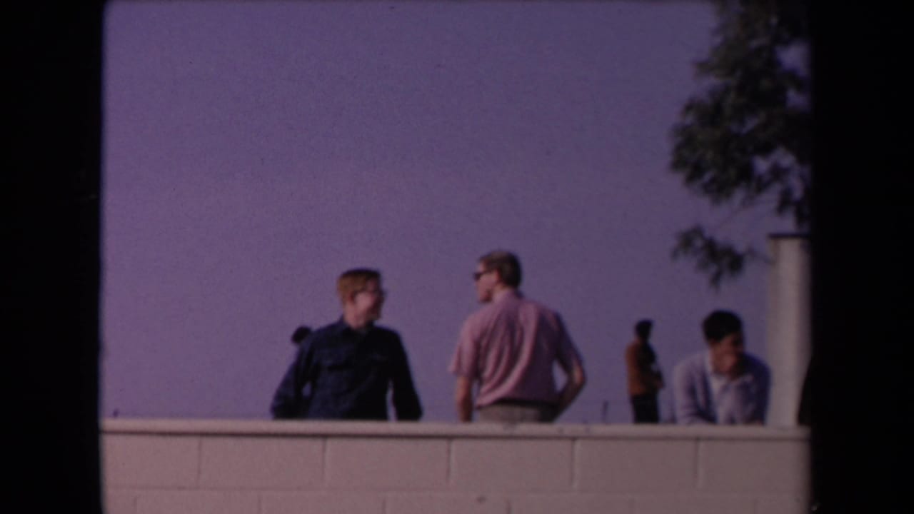 Los Angeles 1967 parade-area view with men on a raised vantage point, a low wall, trees, and a distant uniformed figure.