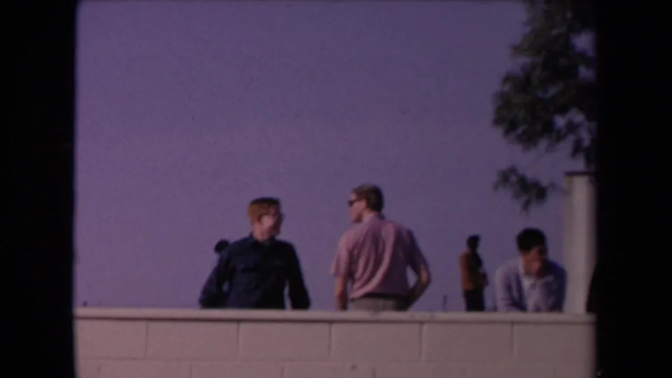 Los Angeles 1967 parade-area view with men on a raised vantage point, a low wall, trees, and a distant uniformed figure.
