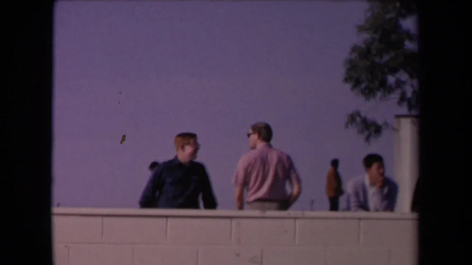 1967 8mm frame of young men watching from behind a low wall in Los Angeles during the Tournament of Roses setting.