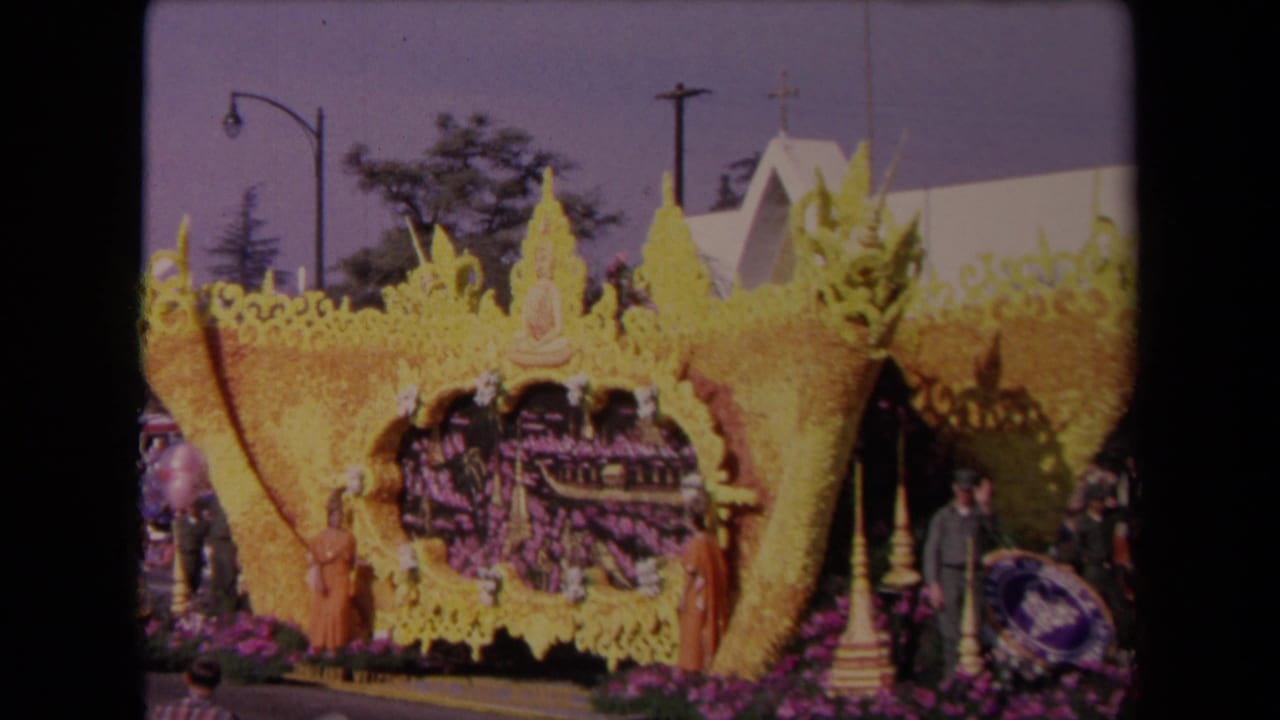 1967 Los Angeles 8mm frame showing an ornate yellow floral parade float with a Buddha figure, purple flowers, and people nearby.
