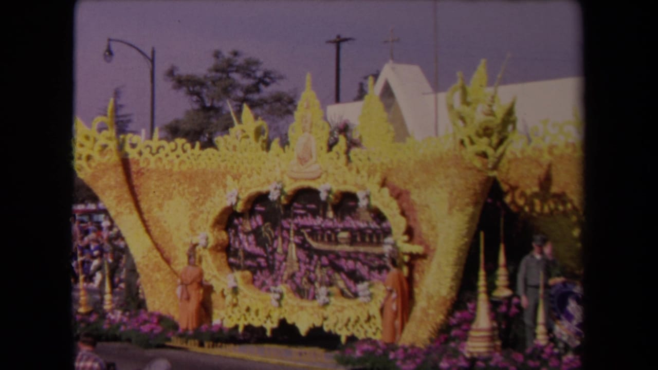 Decorated yellow parade float with Buddha figure, flowers, and onlookers.