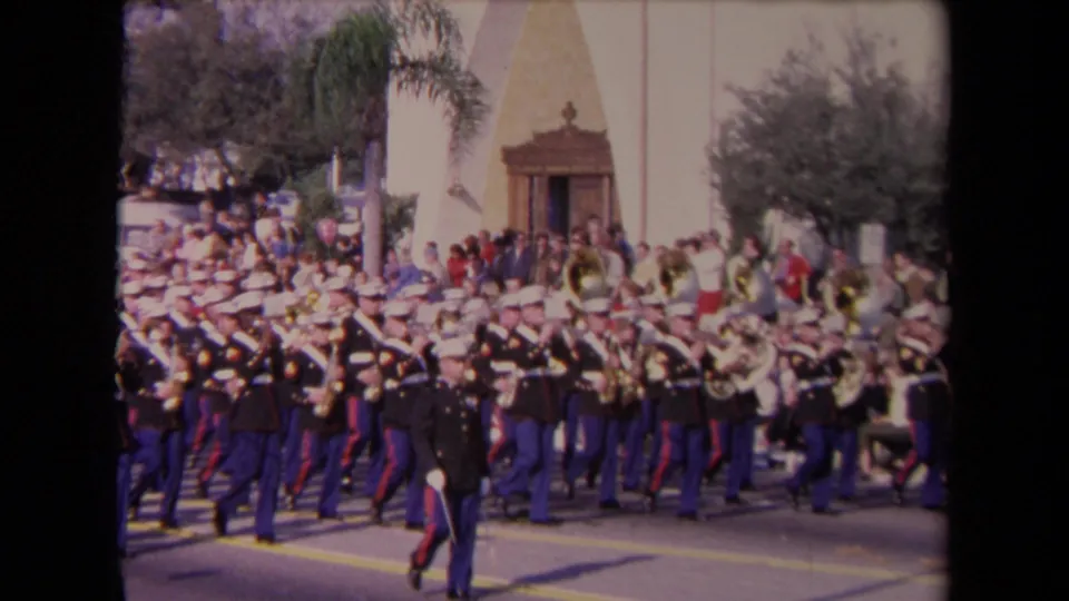 1967 Los Angeles parade footage shows a United States Marine Corps band marching past spectators near a building entrance and palm trees.