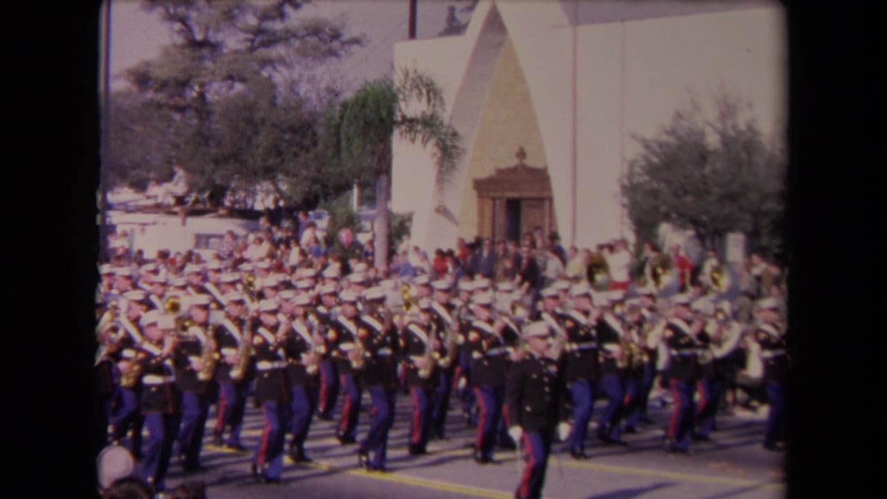 Uniformed Marine musicians march in formation with brass instruments.