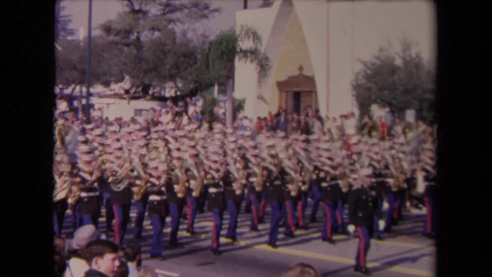 A large Marine band fills the street during the 1967 Los Angeles parade, with spectators and trees behind the formation.