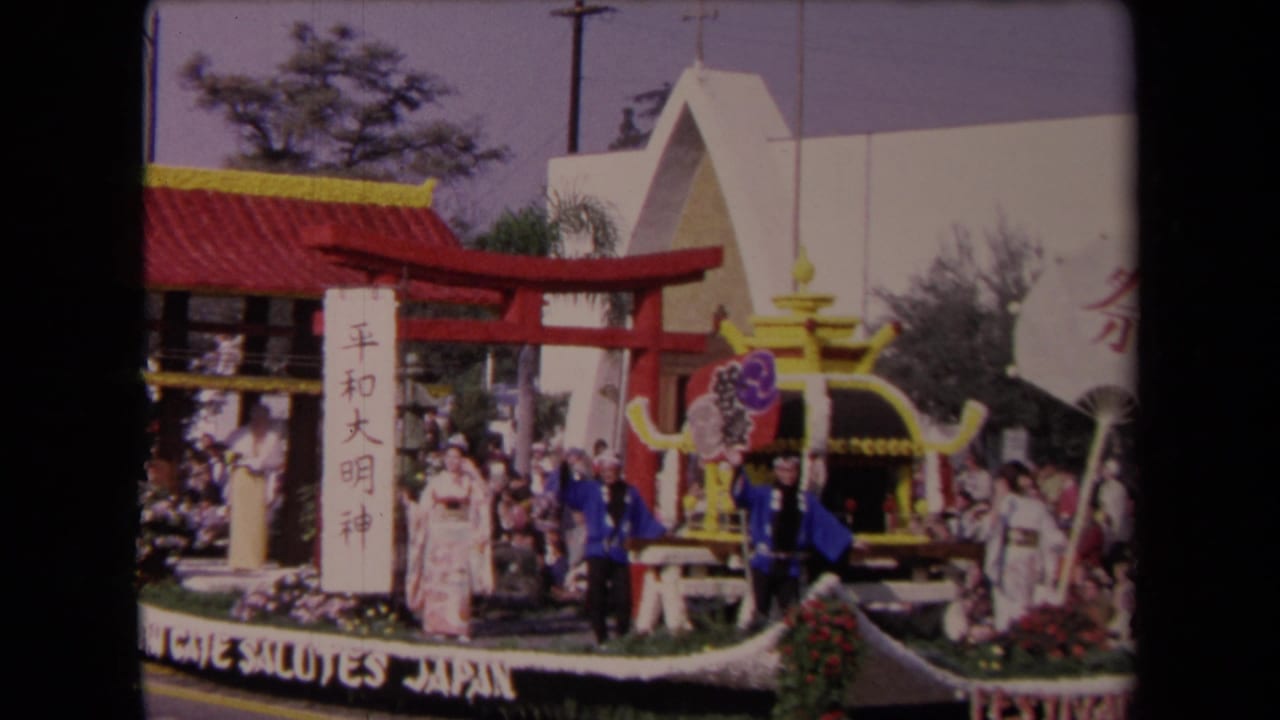 1967 Los Angeles parade float saluting Japan with a red torii gate, pavilion roof, floral trim, participants in kimonos, and spectators nearby.