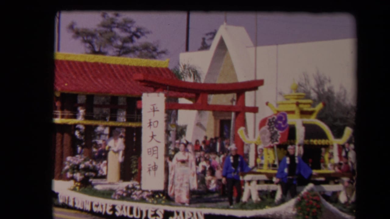 Japan-themed float with torii gate, vertical sign, flowers, pavilion roof, and people in traditional dress.