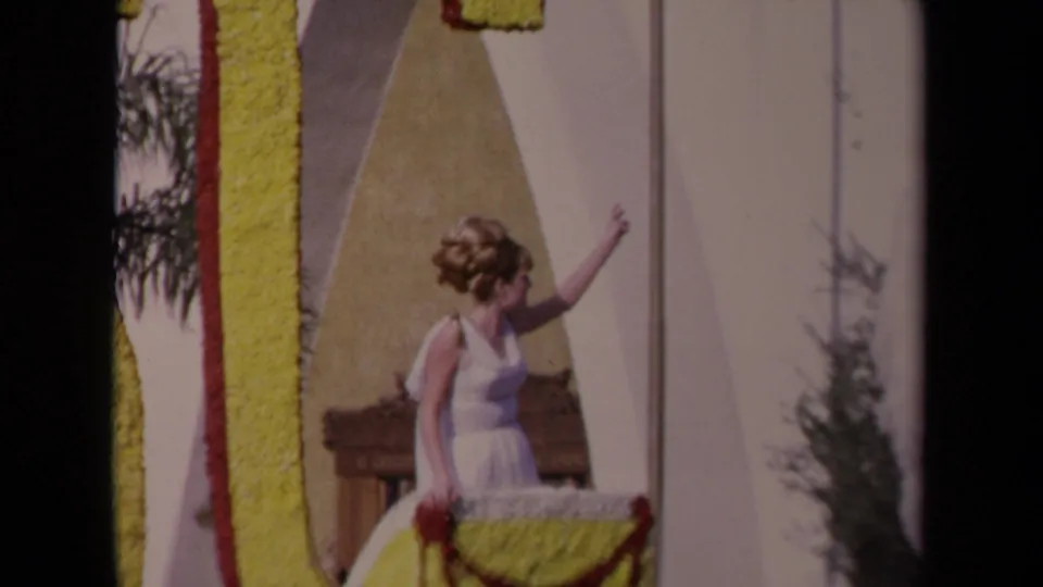 1967 Los Angeles parade view of a woman waving from a decorated float, with yellow display lettering, floral trim, and a white horse figure.