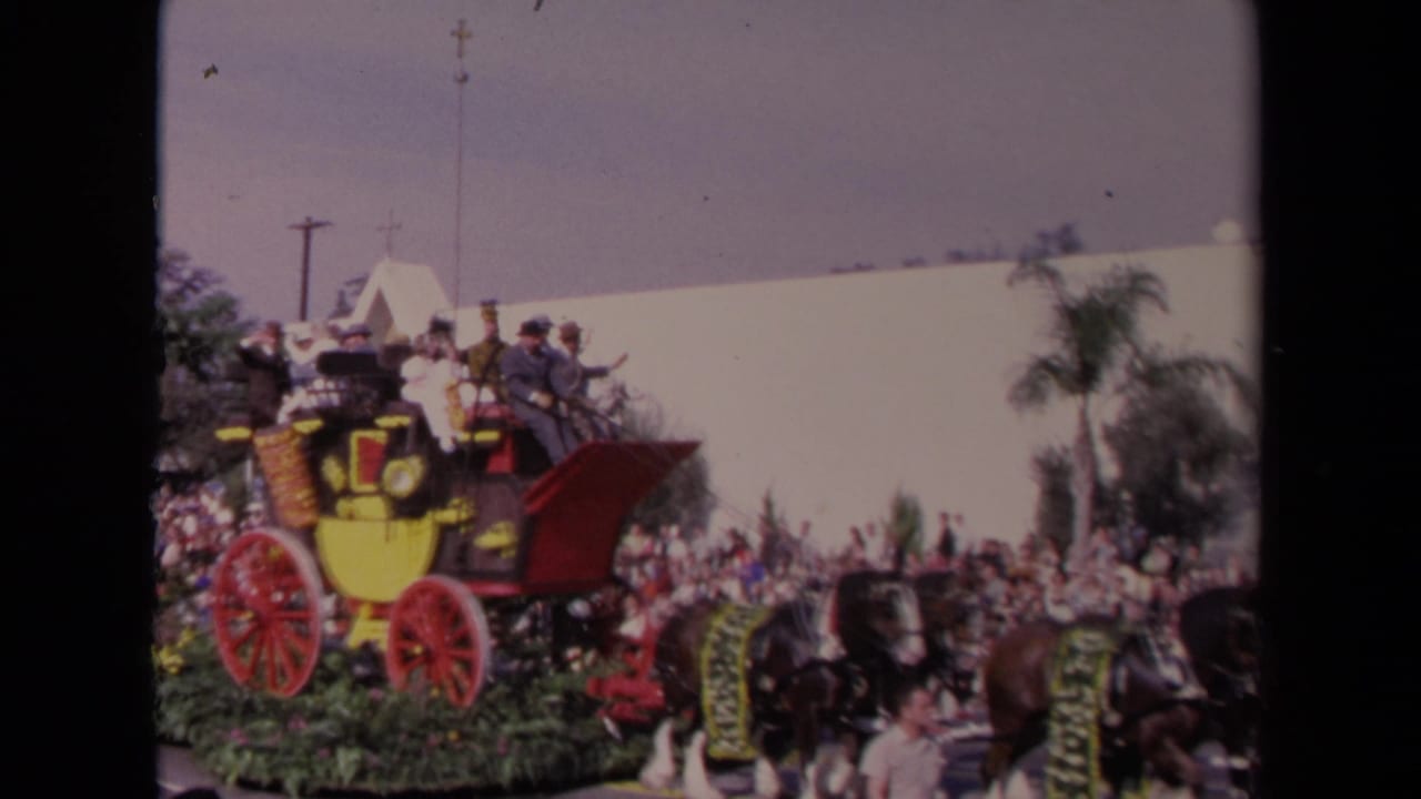 1967 Los Angeles parade frame showing a red-and-yellow stagecoach float pulled by decorated horses before spectators.
