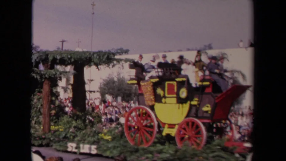 Side view of the 1967 Los Angeles stagecoach float, with riders above red wheels and spectators visible behind parade greenery.